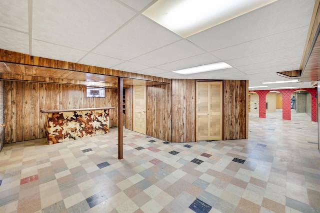 basement with a drop ceiling and wood walls