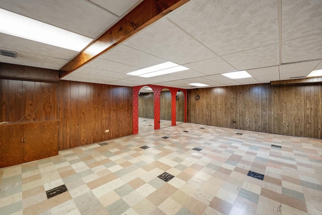 basement featuring a drop ceiling and wooden walls