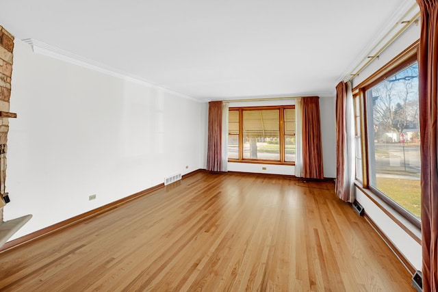 spare room featuring a fireplace, a wealth of natural light, crown molding, and light hardwood / wood-style flooring