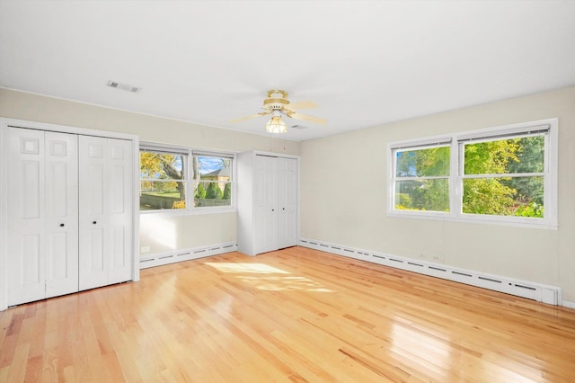 unfurnished bedroom featuring light hardwood / wood-style flooring, multiple windows, and a baseboard heating unit