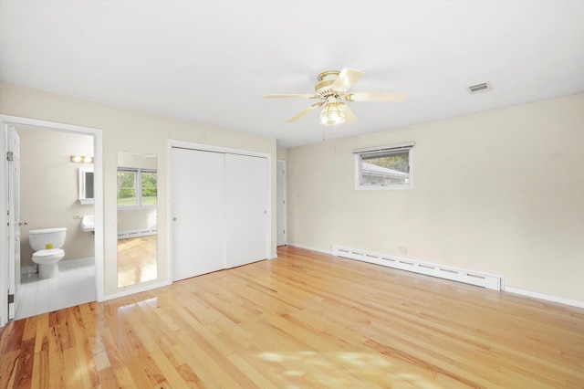 unfurnished bedroom with a baseboard heating unit, ensuite bathroom, ceiling fan, light wood-type flooring, and a closet