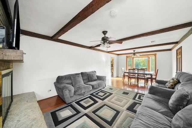 living room with beamed ceiling, wood-type flooring, a brick fireplace, and ceiling fan