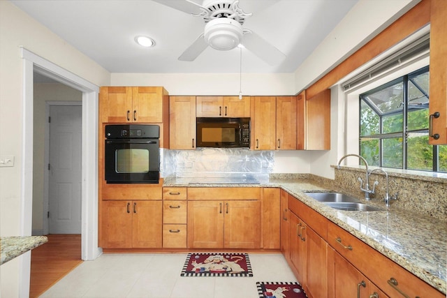 kitchen featuring black appliances, sink, ceiling fan, light stone countertops, and light wood-type flooring