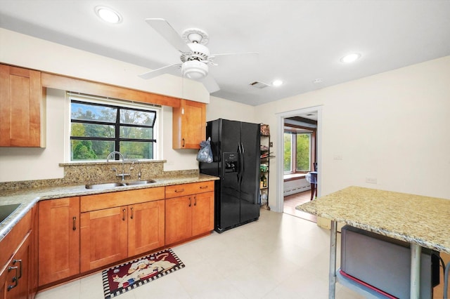 kitchen with a baseboard heating unit, sink, ceiling fan, light stone countertops, and black fridge with ice dispenser