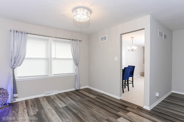 empty room with dark hardwood / wood-style floors and a notable chandelier