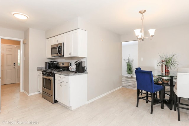 kitchen featuring white cabinets, appliances with stainless steel finishes, decorative light fixtures, light stone counters, and a chandelier