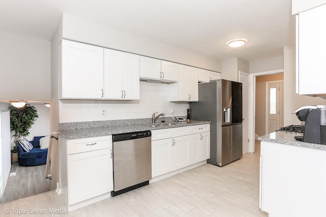 kitchen with light stone counters, stainless steel appliances, white cabinetry, and sink