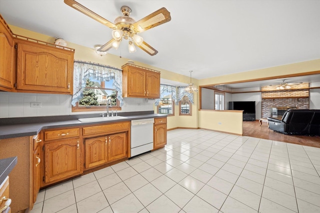 kitchen with sink, backsplash, white dishwasher, a fireplace, and light tile patterned floors