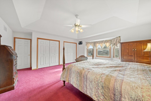 bedroom featuring ceiling fan, a raised ceiling, light carpet, and multiple closets