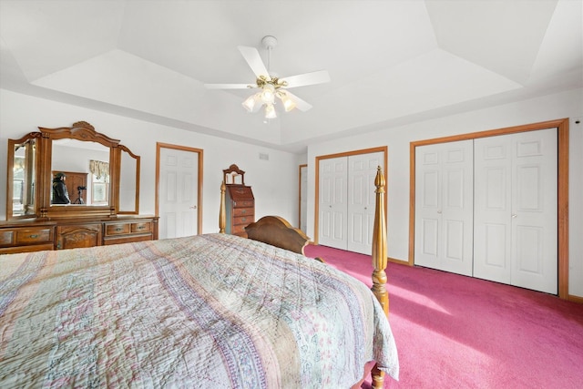 bedroom featuring a raised ceiling, multiple closets, ceiling fan, and carpet floors