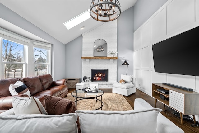 living room featuring a notable chandelier, vaulted ceiling with skylight, dark hardwood / wood-style floors, and a brick fireplace