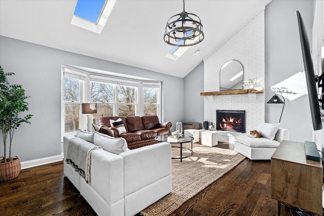 living room featuring dark wood-type flooring, vaulted ceiling with skylight, and a brick fireplace