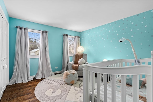 bedroom featuring a closet, a nursery area, dark hardwood / wood-style flooring, and multiple windows