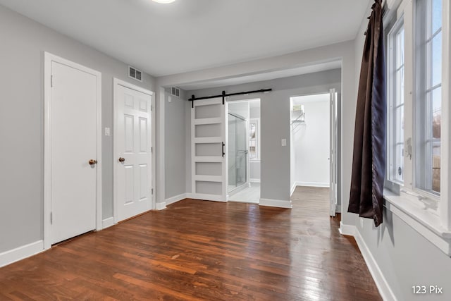 unfurnished bedroom featuring connected bathroom, a barn door, dark wood-type flooring, and multiple windows