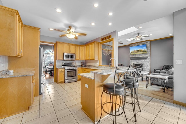 kitchen with a skylight, light stone countertops, a kitchen breakfast bar, kitchen peninsula, and appliances with stainless steel finishes