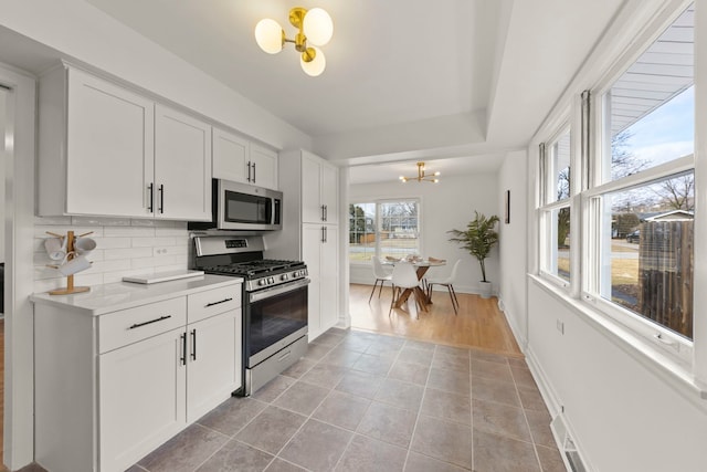 kitchen with tasteful backsplash, white cabinets, stainless steel appliances, a chandelier, and light tile patterned flooring