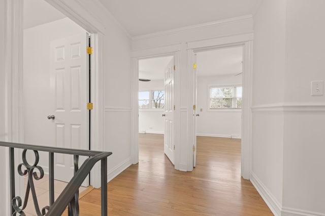 hall featuring baseboards, light wood-type flooring, and crown molding