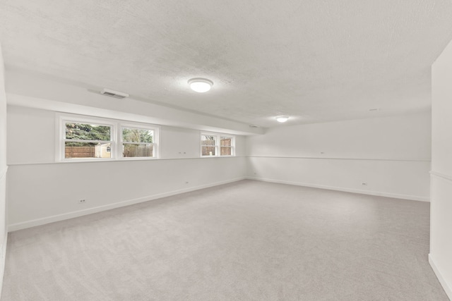 carpeted empty room with a textured ceiling, visible vents, and baseboards