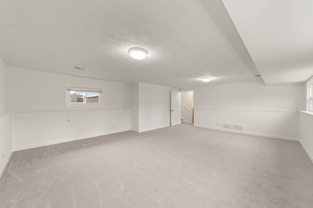 basement with a textured ceiling, baseboards, visible vents, and light colored carpet