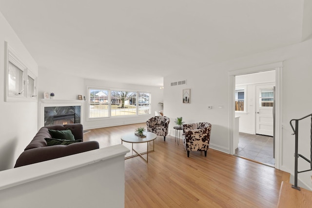 living area with light wood-type flooring, a premium fireplace, and visible vents