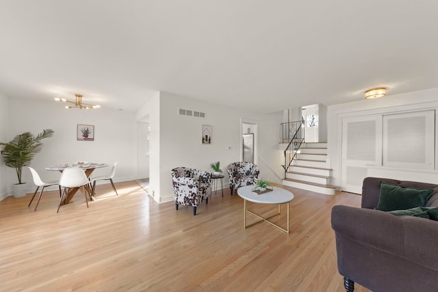 living room with light wood-style flooring, a notable chandelier, visible vents, baseboards, and stairs