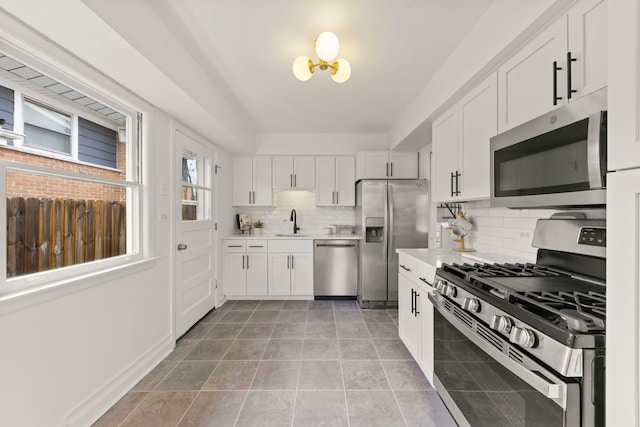 kitchen with stainless steel appliances, a sink, white cabinetry, light countertops, and backsplash