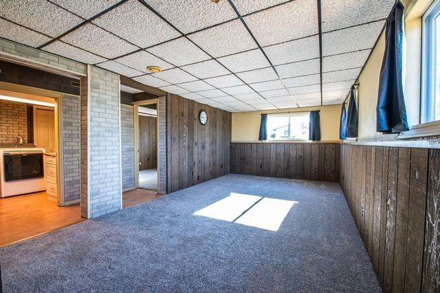 carpeted spare room with wood walls and a drop ceiling