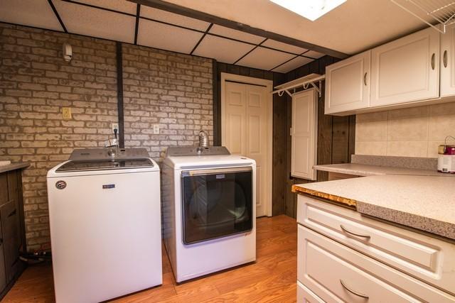 clothes washing area with cabinets, light wood-type flooring, separate washer and dryer, and brick wall