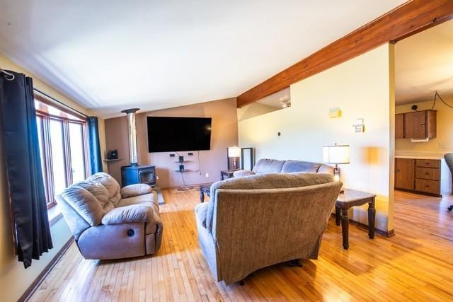 living room featuring a wood stove, lofted ceiling with beams, and light hardwood / wood-style flooring