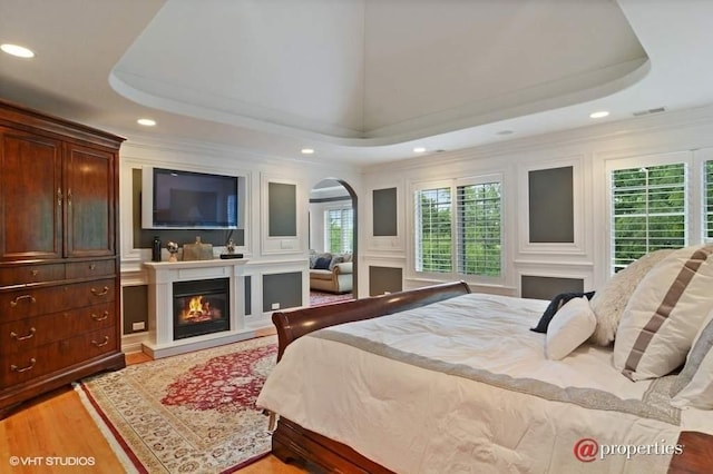 bedroom with wood-type flooring, ornamental molding, a large fireplace, and a raised ceiling