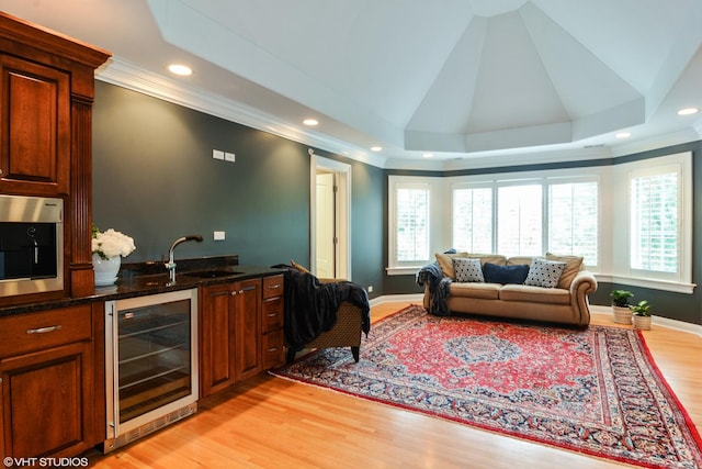 interior space featuring ornamental molding, beverage cooler, a raised ceiling, and light hardwood / wood-style flooring