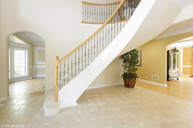 staircase featuring a towering ceiling, ornamental molding, and wood-type flooring