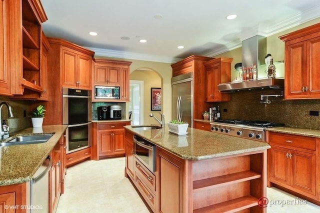 kitchen featuring sink, built in appliances, extractor fan, and a center island with sink