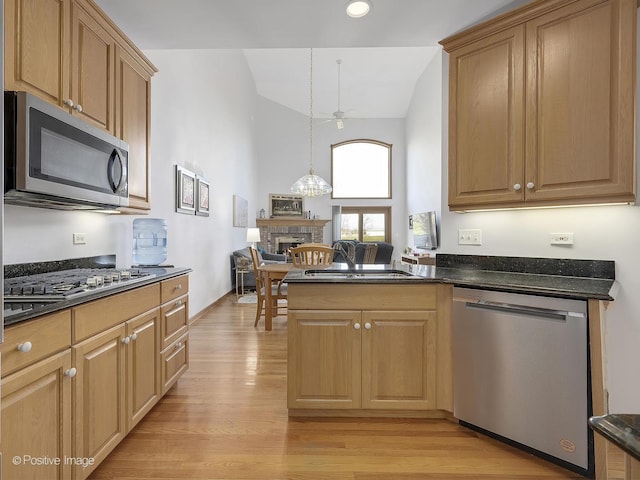 kitchen featuring stainless steel appliances, a stone fireplace, decorative light fixtures, lofted ceiling, and light wood-type flooring