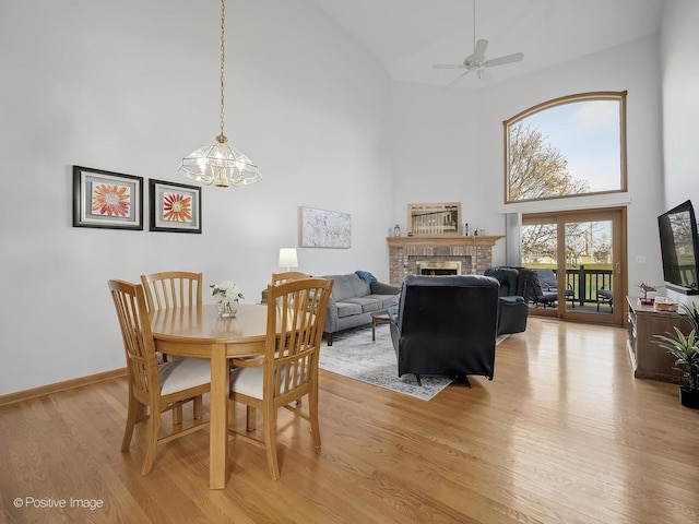 dining space featuring ceiling fan with notable chandelier, light wood-type flooring, a fireplace, and a high ceiling