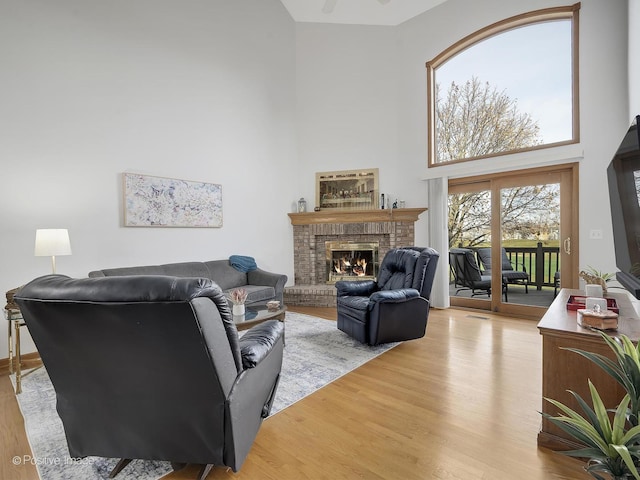 living room featuring a towering ceiling, light hardwood / wood-style flooring, a brick fireplace, and ceiling fan