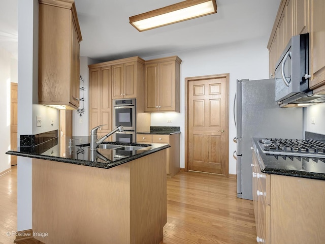 kitchen featuring kitchen peninsula, appliances with stainless steel finishes, dark stone counters, sink, and light hardwood / wood-style floors