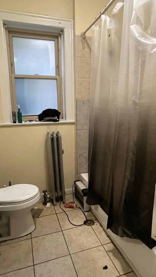 bathroom with tile patterned flooring, shower / bath combination with curtain, toilet, and radiator