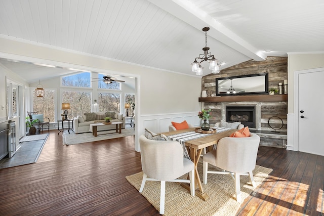 dining space featuring lofted ceiling with beams, a fireplace, wainscoting, dark wood finished floors, and crown molding