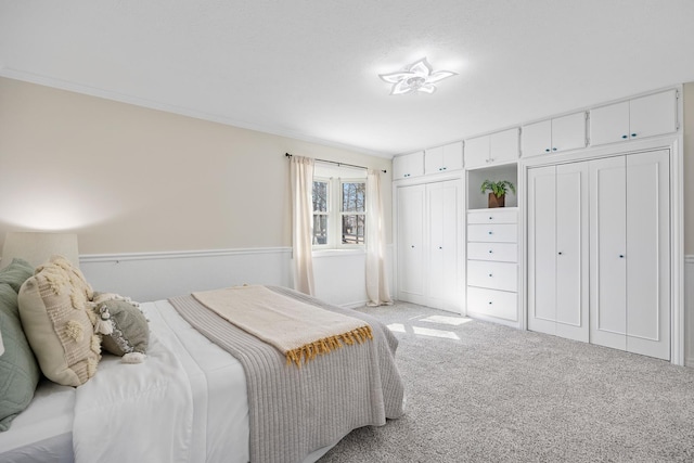 bedroom with ornamental molding, two closets, and light colored carpet