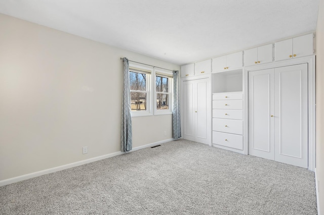 unfurnished bedroom featuring multiple closets, light carpet, visible vents, and baseboards