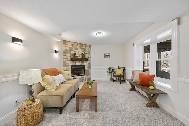 living room with a textured ceiling, a stone fireplace, a decorative wall, wainscoting, and carpet