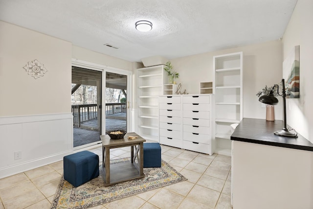 interior space featuring a wainscoted wall, visible vents, a textured ceiling, and light tile patterned flooring