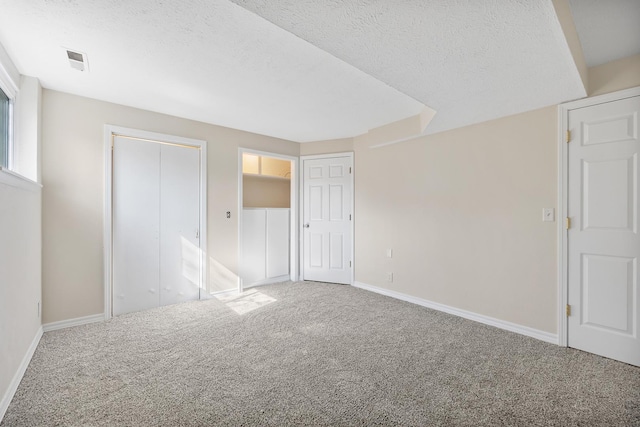 unfurnished bedroom with a textured ceiling, carpet flooring, visible vents, and baseboards