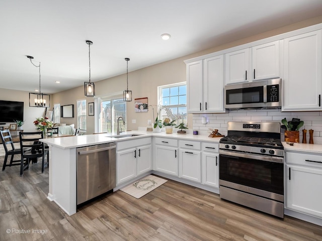 kitchen with appliances with stainless steel finishes, sink, decorative light fixtures, light hardwood / wood-style flooring, and white cabinets