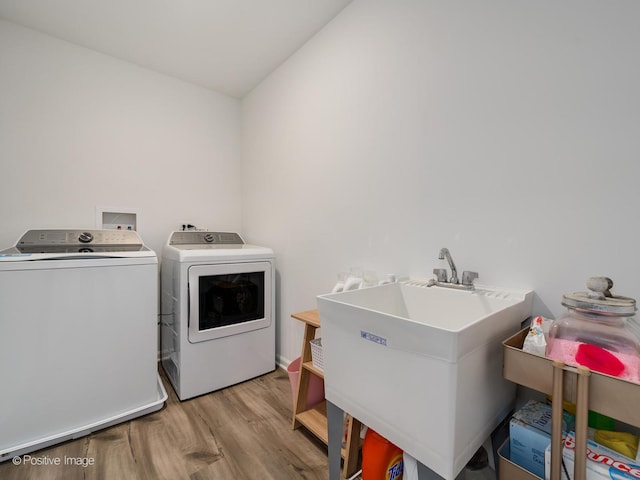 laundry area featuring independent washer and dryer, sink, and light hardwood / wood-style flooring