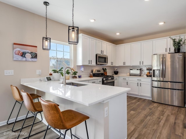 kitchen with white cabinetry, sink, stainless steel appliances, dark hardwood / wood-style floors, and kitchen peninsula