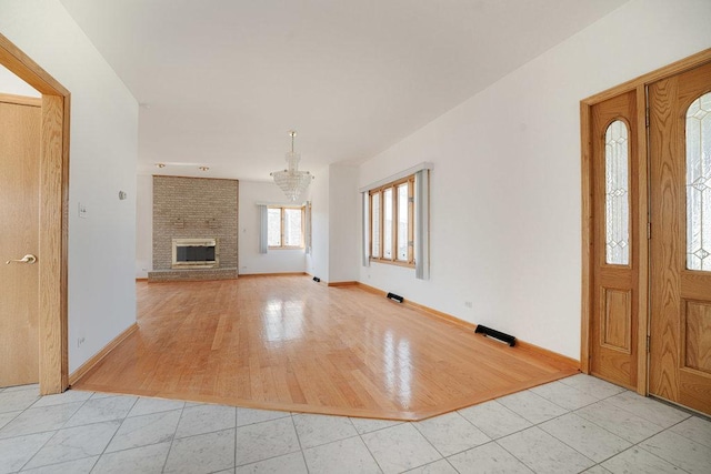 foyer entrance with tile patterned flooring, a brick fireplace, a notable chandelier, and baseboards