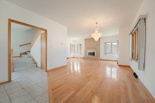 unfurnished living room featuring light wood-style floors, a notable chandelier, baseboards, and stairs