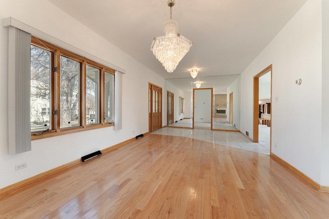 unfurnished room featuring a notable chandelier, baseboards, and light wood-style floors